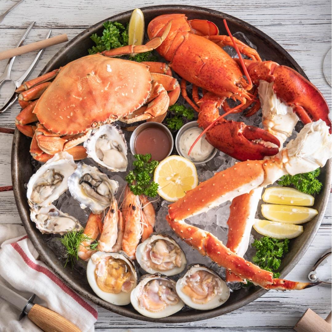 Fresh seafood platter featuring crab, lobster, king crab legs, oysters, shrimp, and clams on ice